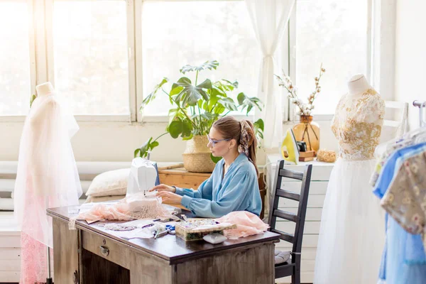 Glimlachend jonge naaister vrouw naait kleding op een naaimachine in haar atelier — Stockfoto