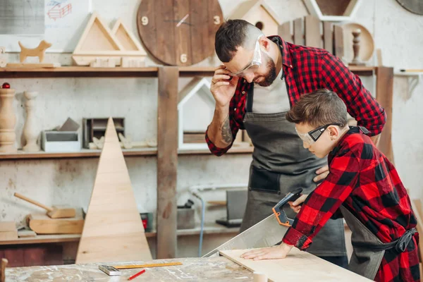 Папа с сыном работают в мастерской, распиливают деревянные доски  . — стоковое фото