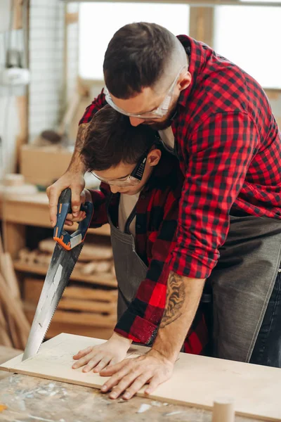 Papá y su hijo están trabajando en el taller. Están aserrando tablones de madera . —  Fotos de Stock