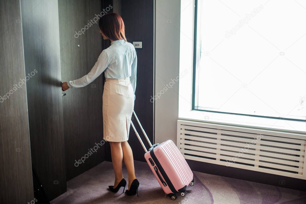 Elegant woman speaking on smart phone while leaving hotel with suitcase.