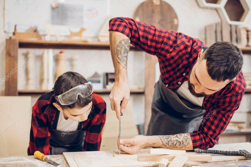 Father and son in workshop tinkering wooden toy. Dad teaching little son to repair. Fatherhood and sharing of experience concept. Teacher with male kid working with tool, using screwdriver