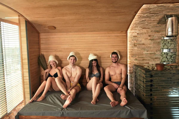 Dois casais heterossexuais tendo um banho de sauna em uma sala de vapor com vassouras de carvalho — Fotografia de Stock