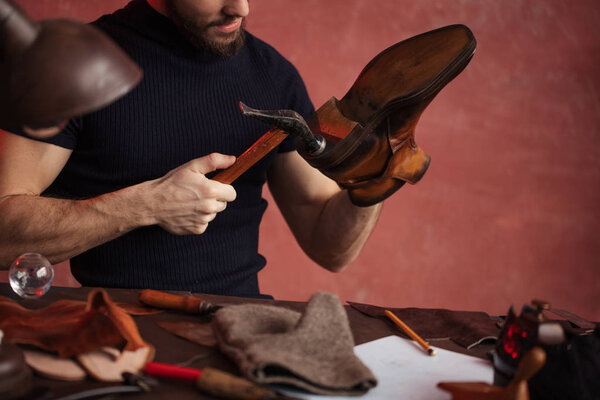 close-up cropped photo of shoemaker repairing shoes by nailing a heel