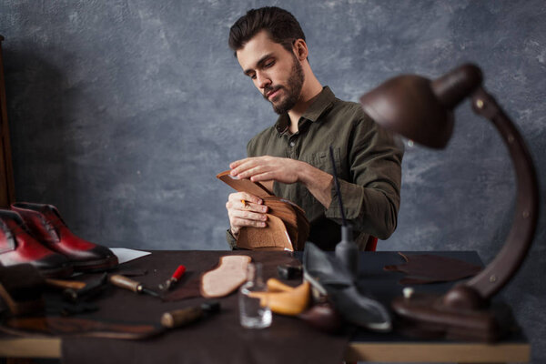 young awesome craftsman working with different kinds of leather