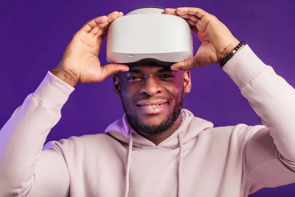 Afrikaanse man draagt virtual reality bril geïsoleerd op donker paarse achtergrond — Stockfoto