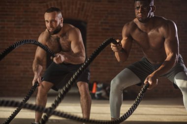 Birlikte savaş ipler spor salonunda egzersiz iki çok ırklı çıplak göğüs sporcular.