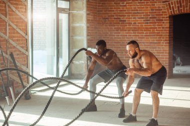 Birlikte savaş ipler spor salonunda egzersiz iki çok ırklı çıplak göğüs sporcular.
