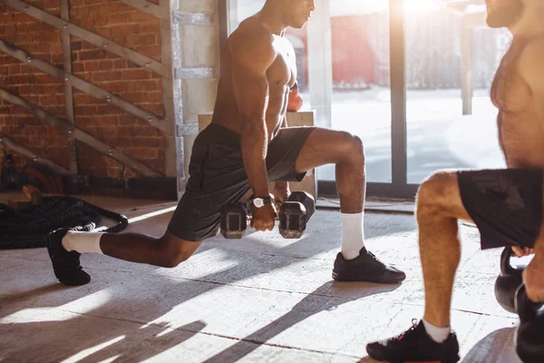 Twee multiraciale mannelijke atleten maken lunges met gewicht in indoor training — Stockfoto