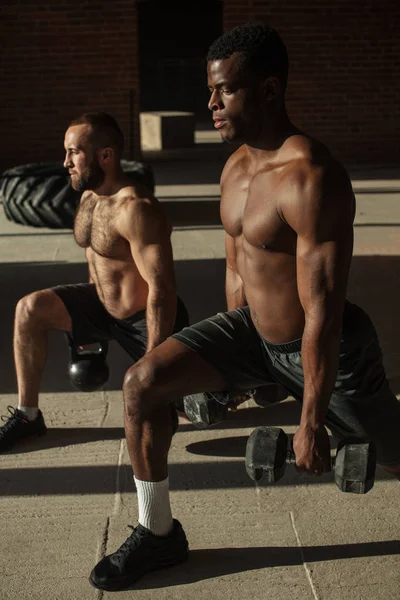 Twee multiraciale mannelijke atleten maken lunges met gewicht in indoor training — Stockfoto