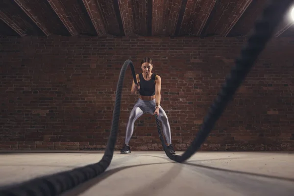 Joven mujer caucásica haciendo ejercicio con cuerdas de batalla en un gimnasio — Foto de Stock