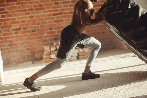 Athletic african american man exercising with tyre and looking away in gym