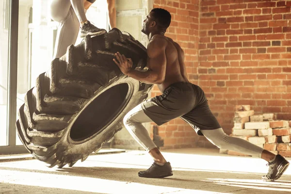 African man flipping a tire with a woman on it, working out with weighting