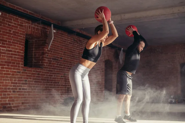 Atletisk ung man och kvinna i sportkläder tränar med medicinbollar i gymmet — Stockfoto