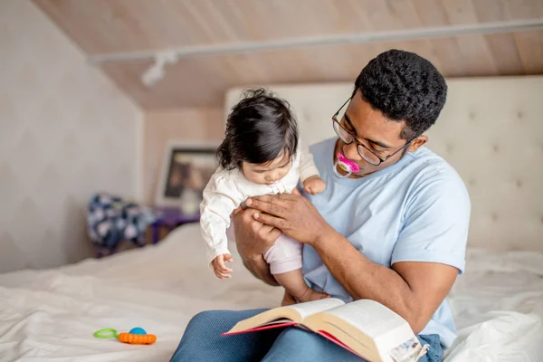 Atractivo hombre está sosteniendo a una niña y leyendo un libro —  Fotos de Stock