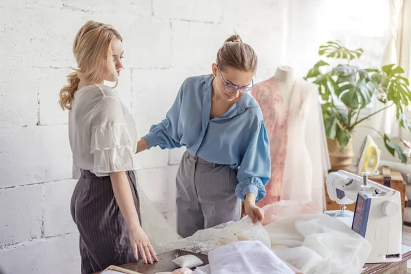 Professional female dressmaker choosing fabric together with attractive woman — Stock Photo, Image