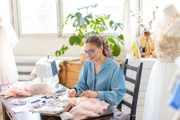 Молодая женщина портной сидит на рабочем месте и выбирает цвет нитей в ателье — стоковое фото
