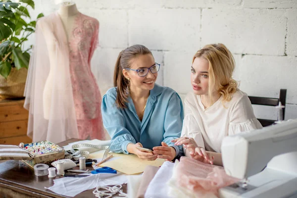 Vrouwelijke naaister ontwerp tonen aan haar cliënt, samen zitten op workshop. — Stockfoto