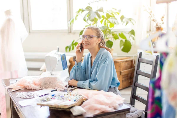 Linda costureira vestindo blusa elegante e óculos falando no telefone — Fotografia de Stock