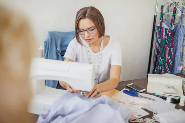 Usmívající se žena mladá švadlena šije oblečení na šicí stroj ve své dílně — Stock fotografie