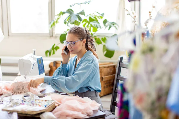 Beautiful seamstress wearing stylish blouse and eyeglasses talking on the phone