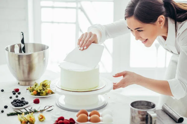 Alegre chica usando un smooother mientras hornear pastel —  Fotos de Stock
