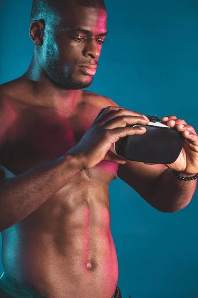Ung afrikansk idrottsman med muskulös kropp håller VR headset på blå, närbild. — Stockfoto