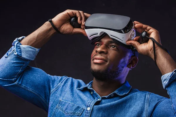 Pozytywny Afrykanin zdejmujący okulary VR z głowy na czarnym tle — Zdjęcie stockowe