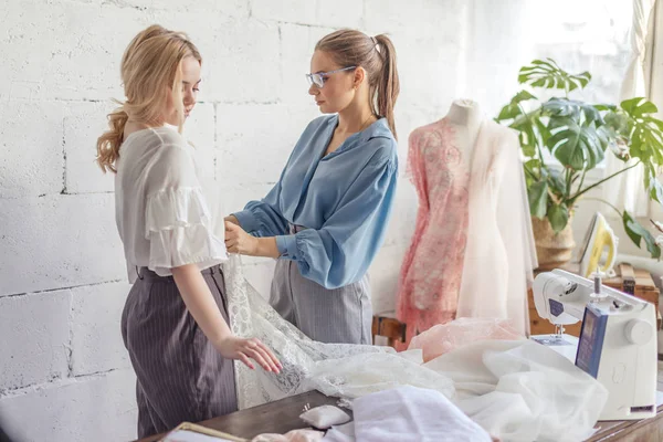 Profissional costureira feminina escolhendo tecido junto com mulher atraente — Fotografia de Stock