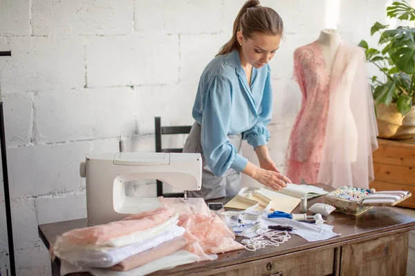 Genç kadın terzi işyerinde oturur ve atelier içinde konu rengini seçer — Stok fotoğraf