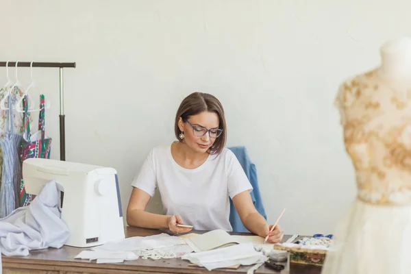 Modedesigner på jobbet. Produkt sömmerska ritning skiss på hennes arbetsyta — Stockfoto