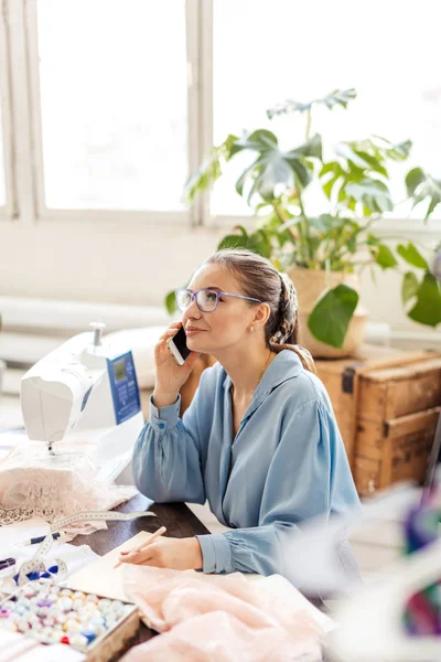 Mooie naaister dragen van stijlvolle blouse en brillen praten aan de telefoon — Stockfoto