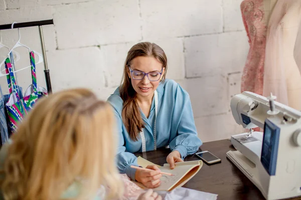 Kvinnliga sömmerska diskuterar funktioner av ordningen med klienten i mysiga studio — Stockfoto