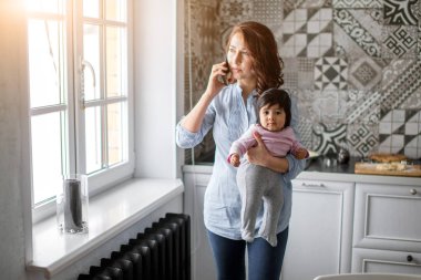 bebeği tutarak ve smartphone üzerinde konuşmak meşgul ciddi anne.