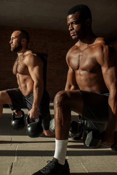 Dos atletas masculinos multirraciales que hacen embestidas con peso en el entrenamiento en interiores —  Fotos de Stock