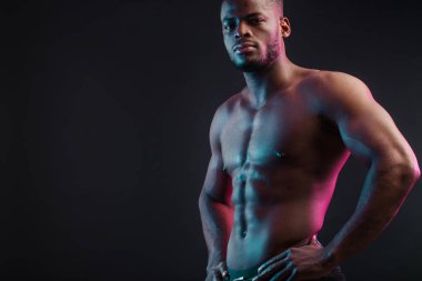 Siyah duvara karşı çıplak poz veren Afrikalı erkek sporcu. Düşük tuşlu fotoğraf.