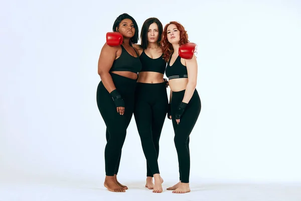 Three multiracial diverse woman in black sportswear posing in boxing gloves — Stock Photo, Image