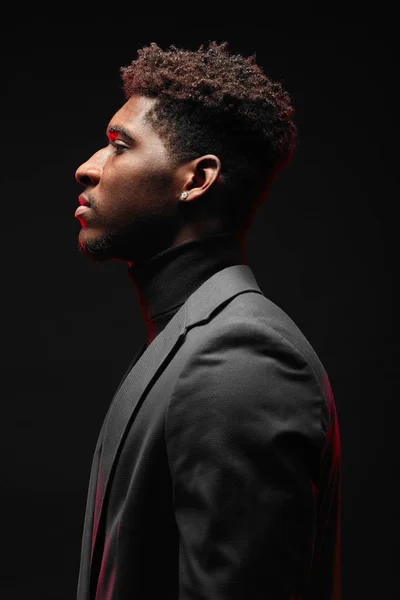 Young dark-skinned entrepreneur in formal clothing, standing against dark wall — Zdjęcie stockowe