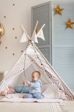 Sevimli çocuk mavi oyun odasında oyuncak çadırıyla oynuyor.