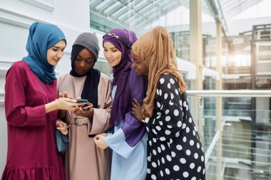 Müslüman çok ırklı kızlar Afrikalı bir kadının elindeki akıllı telefona bakıyorlar.