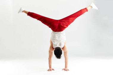 Kırmızı eşofmanlı genç adam beyaz arka planda amuda kalkıyor.