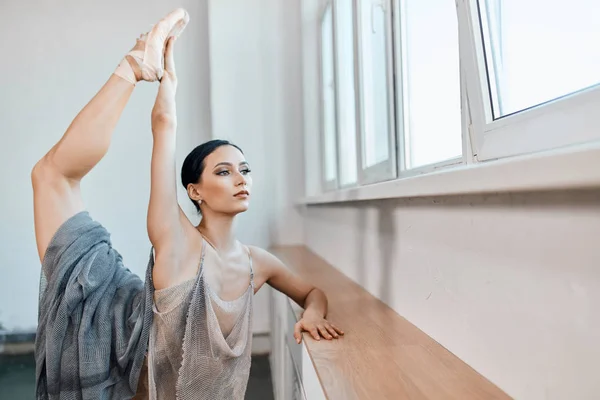 Ballerina standing on one leg on toes in pointe and lifting another one up high. — Stock Photo, Image