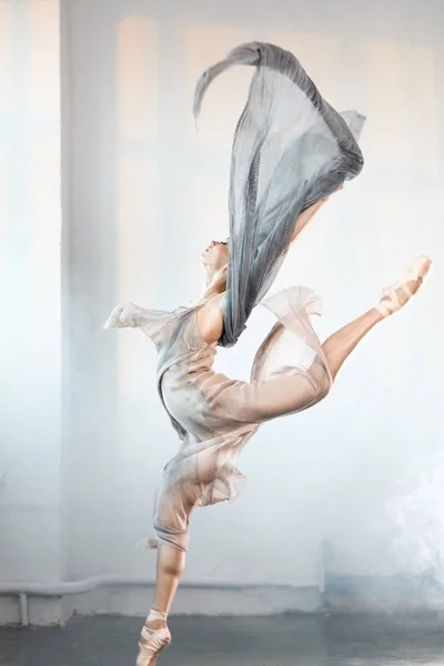 Ballerina s šedými průhlednými oděvy skákající na pódium s kouřovým efektem — Stock fotografie
