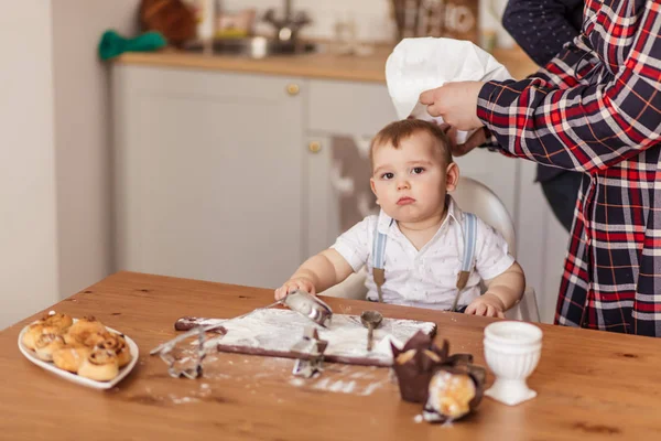 Niño pequeño cocinero ayuda a hacer pasteles sentados a la mesa con harina untada. — Foto de Stock