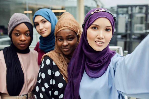 Group of four multiethnic Muslim women in traditional hijab take selfie in mall
