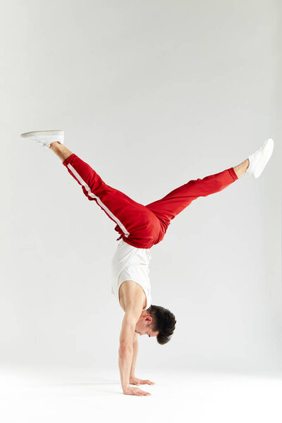 Young man in red sweatpants doing a handstand on hands on white background