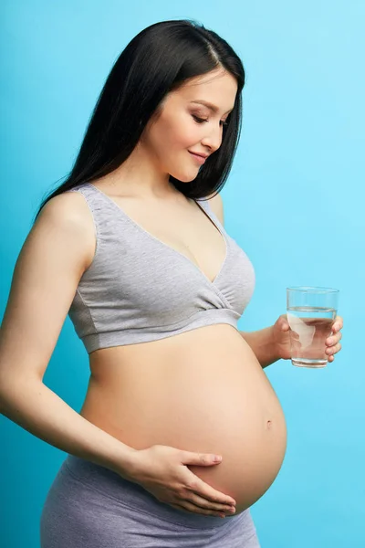 Young undressed pregnant woman with big tummy holding a glass of water — Stock Photo, Image