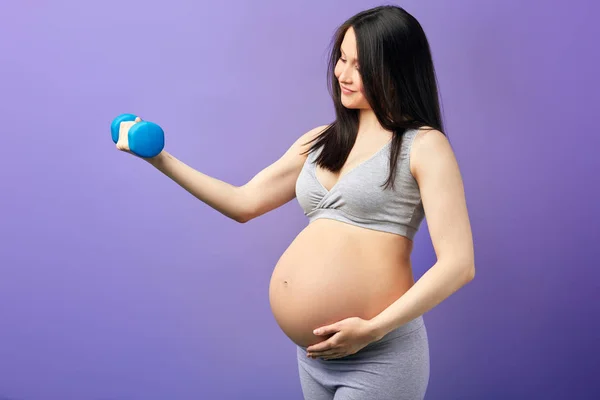 Mama gravidă fericită exercițiu la studio cu gantere pe fundal violet — Fotografie, imagine de stoc