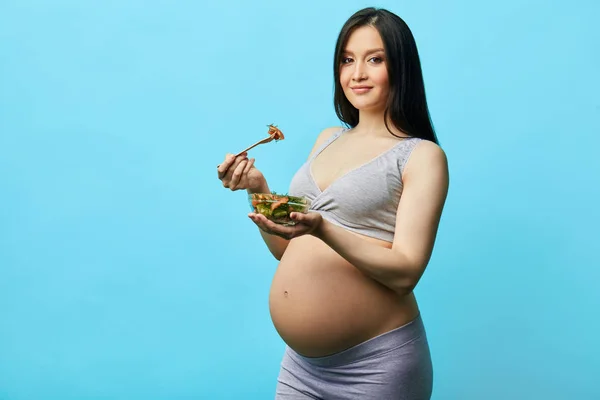 Foto aislada de futura madre joven comiendo alimentos saludables sobre fondo azul — Foto de Stock