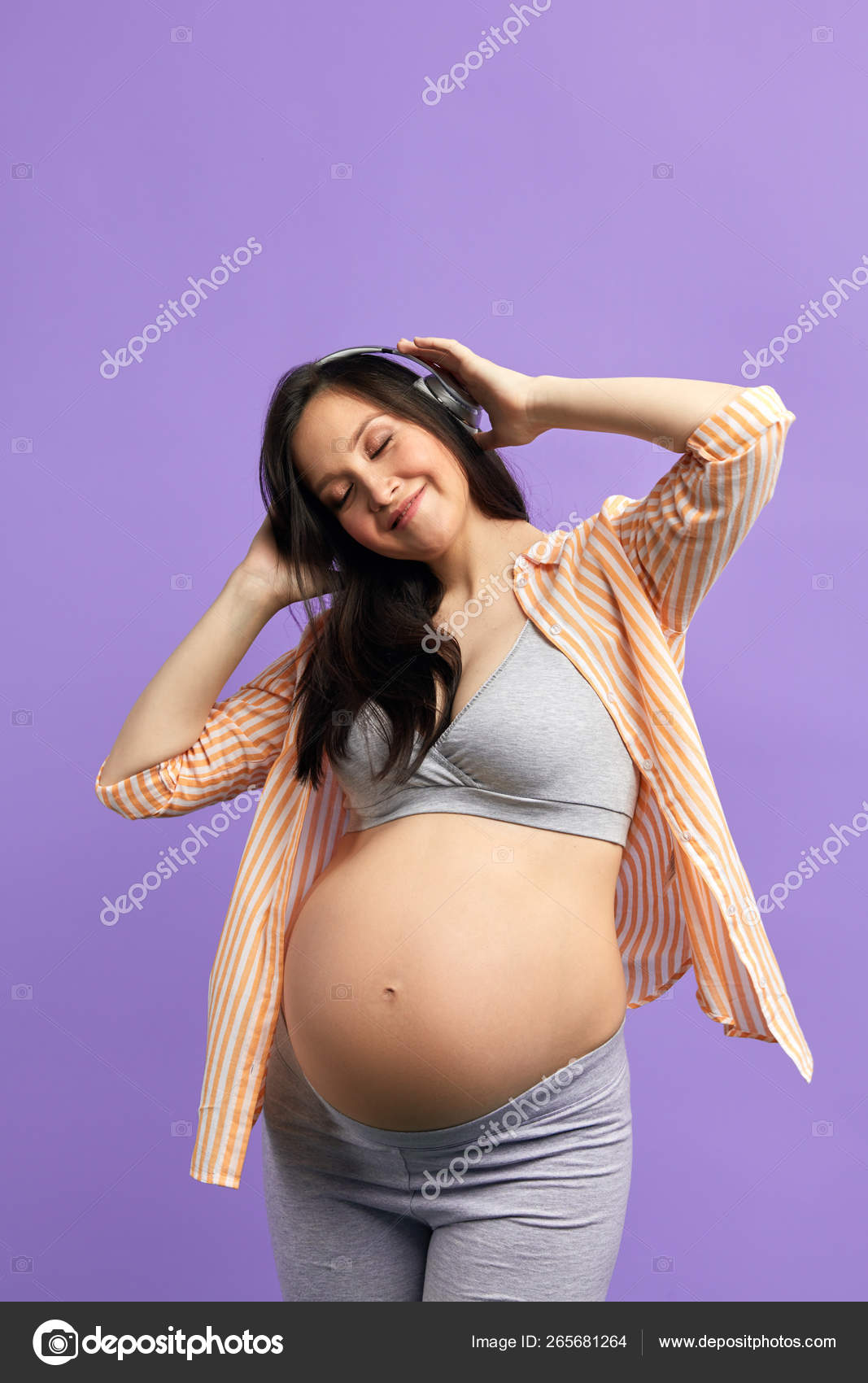 Smiling pregnant woman in headphones dancing in studio over purple  background. Stock Photo by ©ufabizphoto 265681264