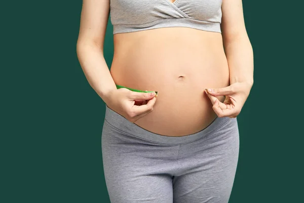 Embarazada en sobremesa mide su vientre desnudo con cinta métrica en verde — Foto de Stock